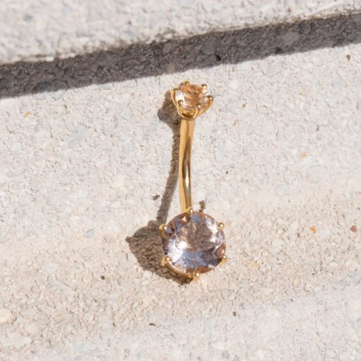 18k yellow gold Orb 8mm Morganite navel ring resting on sunlit stone, the 8mm round morganite catching the light