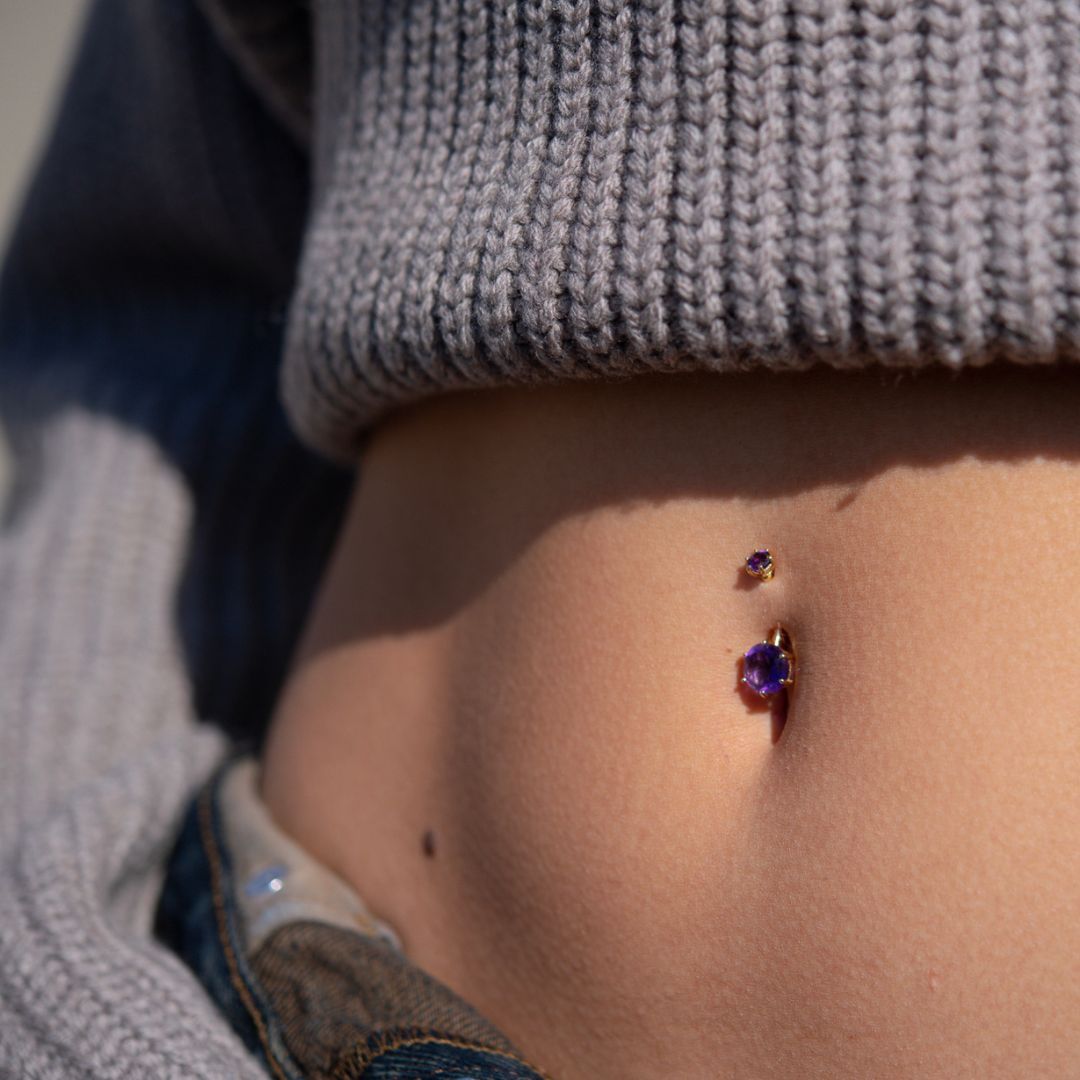 The Orb 8mm Amethyst belly button ring up close, paired with a grey knit sweater